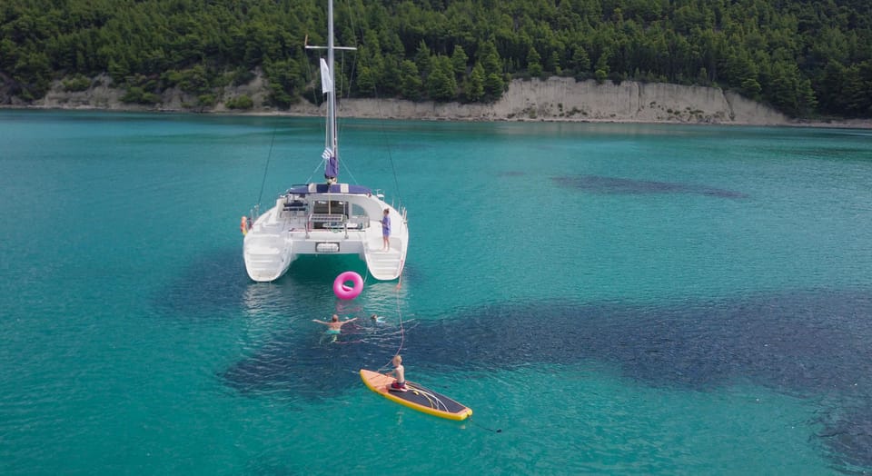 Eight-Hour Lagoon Catamaran from Gouvia: The Live Title Still Says Half Day 1 Lagoon catamaran anchored in a sheltered turquoise bay with a paddleboard astern