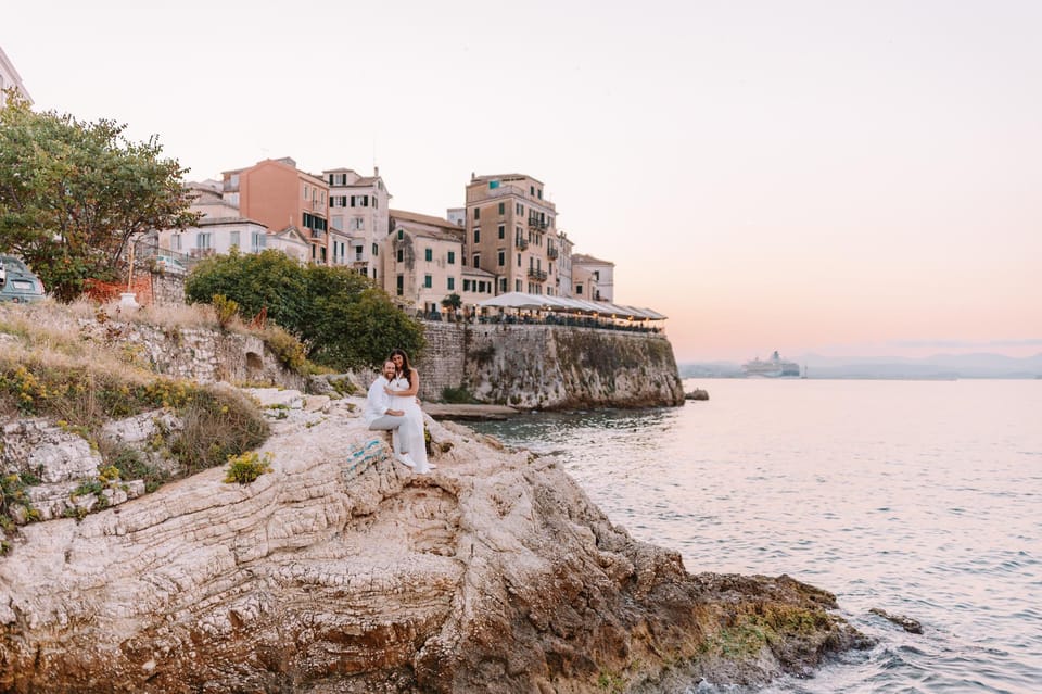 Private Corfu Photoshoot: Choose the Deliverable Before the Backdrop 3 Bride and groom seated on coastal rocks below Corfu Town